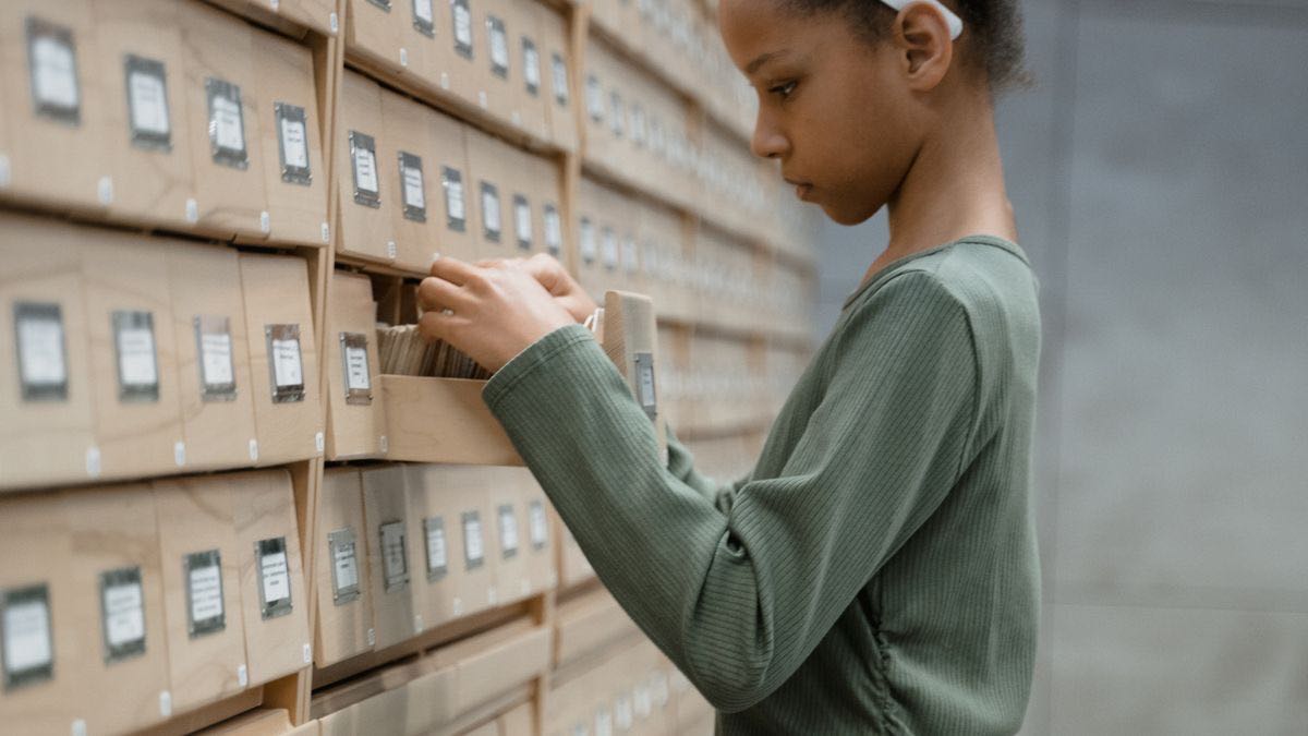 A person pulling a card from a wall of wooden library catalogue drawers, the manual version of tracking AI search citations