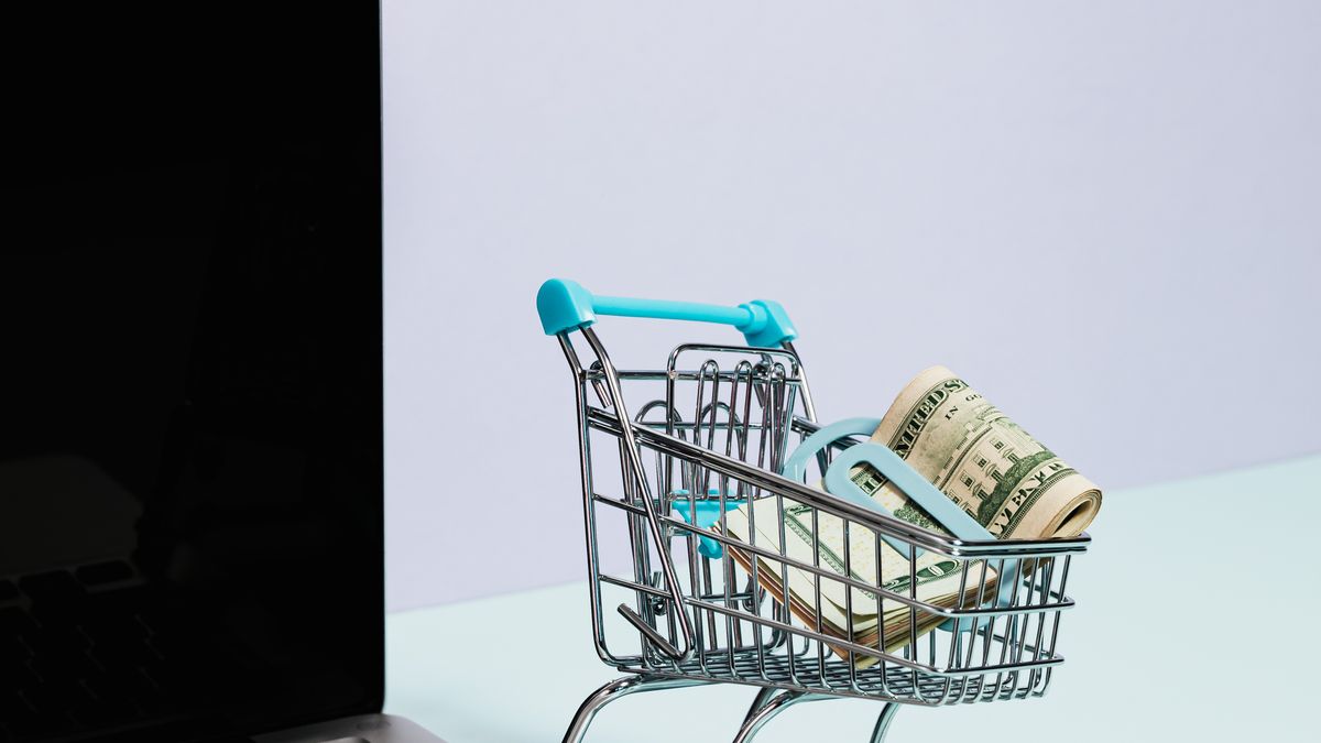 A miniature shopping cart with cash on a laptop, representing a Brave Shopping API for e-commerce price data