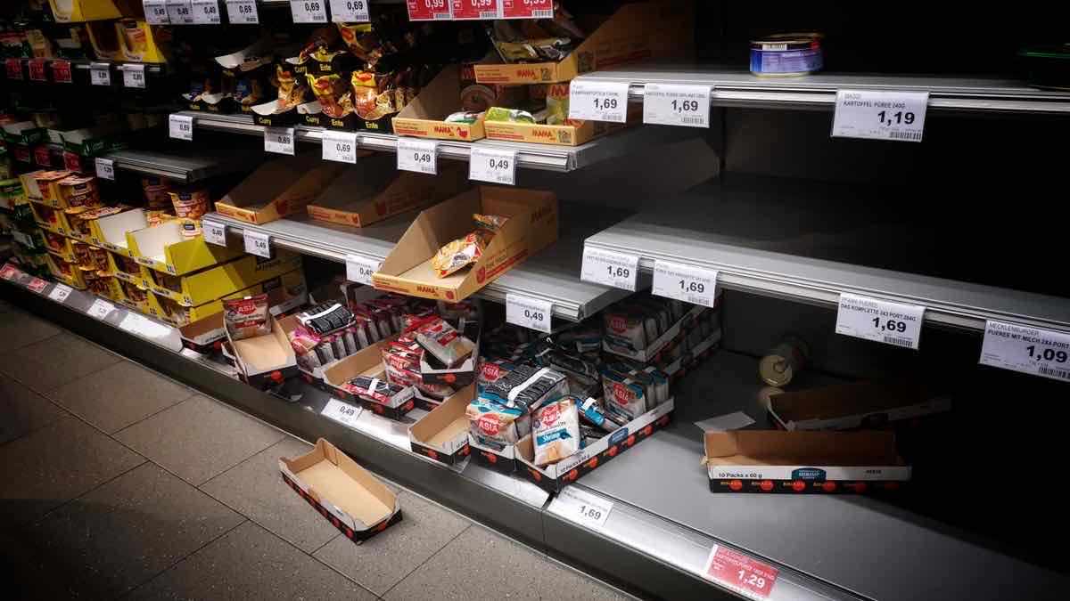 A supermarket aisle photographed from above, price labels along the shelf edge with the stock behind many of them gone