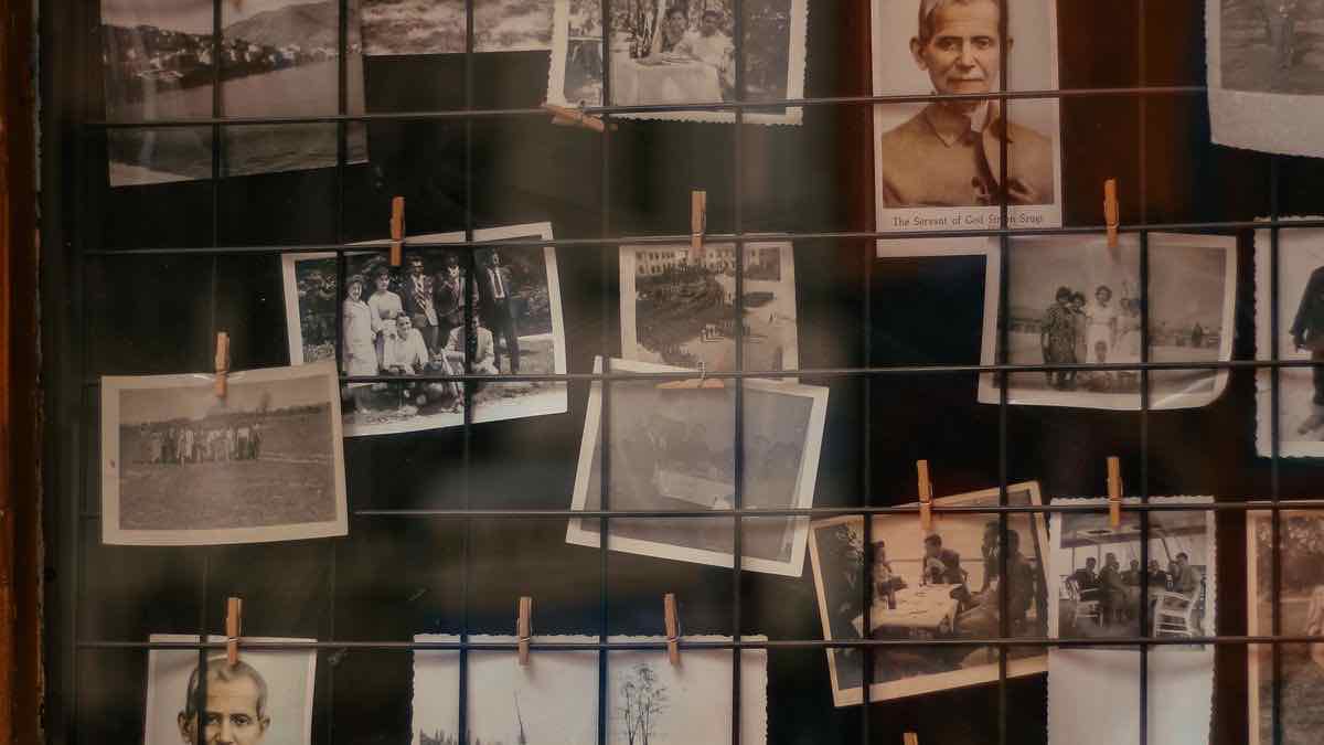 Dozens of old sepia photographs pegged to a wire grid with wooden clothes pegs, seen behind glass
