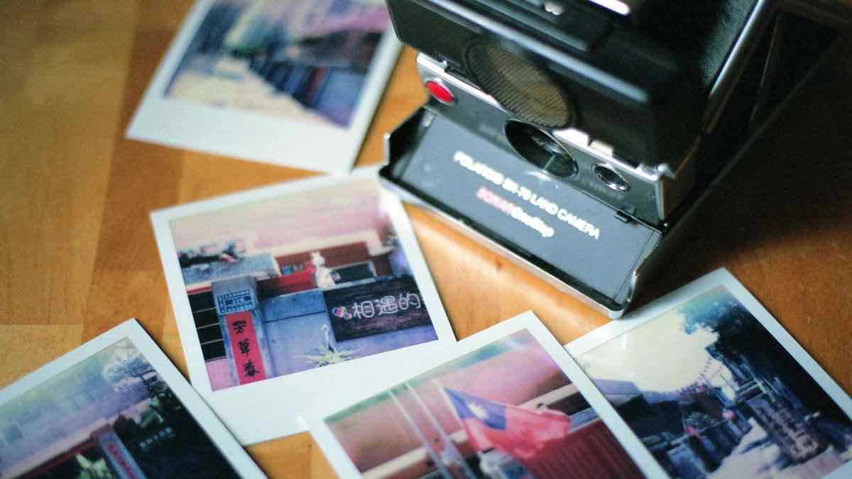 A black Polaroid SX-70 instant camera lying on a wooden floor with four instant prints fanned out around it
