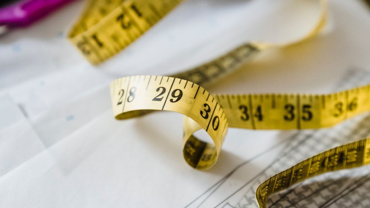 A soft tailor's tape measure curled on a paper sewing pattern, the numbers 28 to 36 in focus