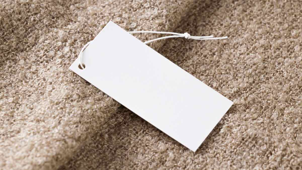 A blank white price tag lying on a woollen surface, with nothing written on it