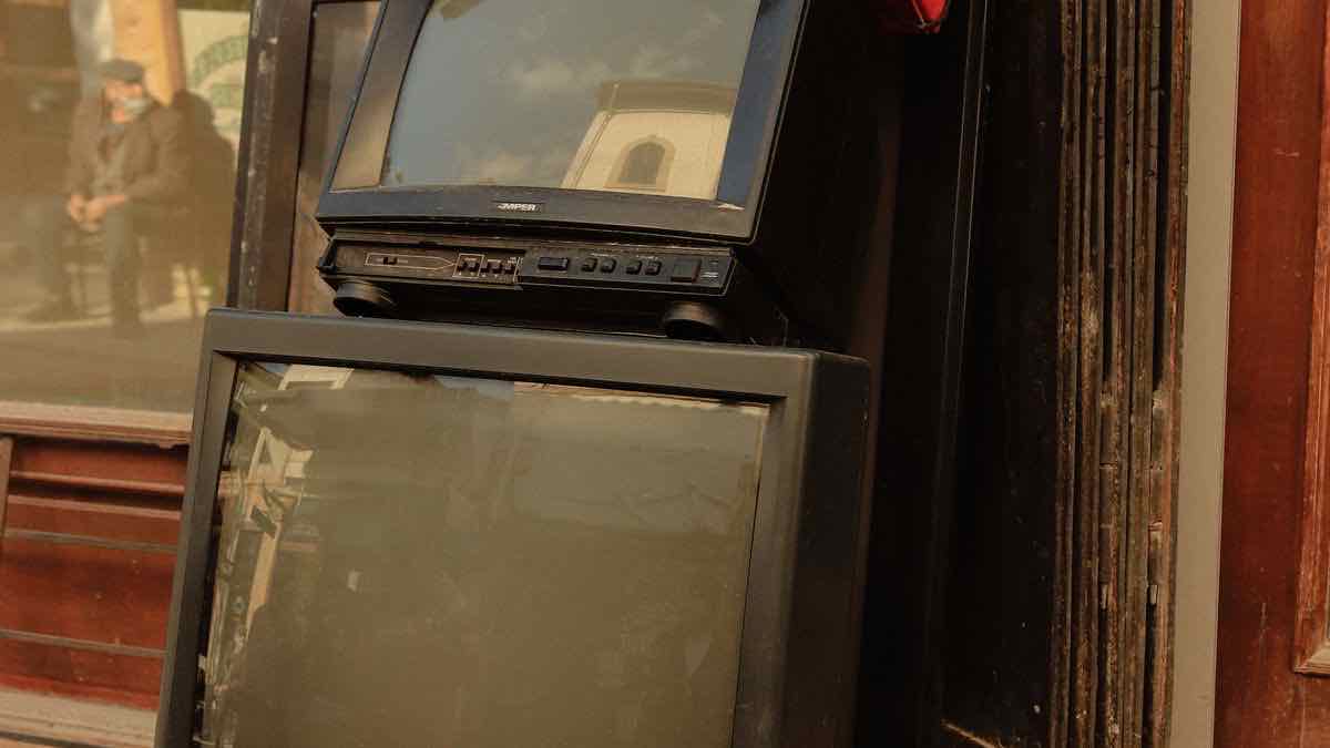 Two dusty CRT televisions stacked in a shop doorway with a street reflected in the glass, a picture of two identical-looking boxes that are sold by different measures