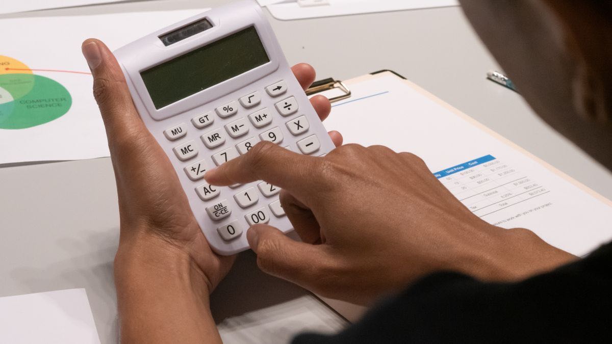 A person working out unit costs on a calculator beside printed pricing sheets and a cost table
