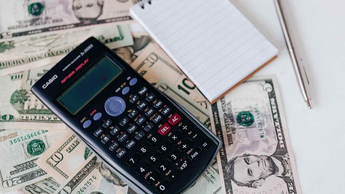 Scientific calculator lying on a spread of US dollar bills next to a notepad and pen