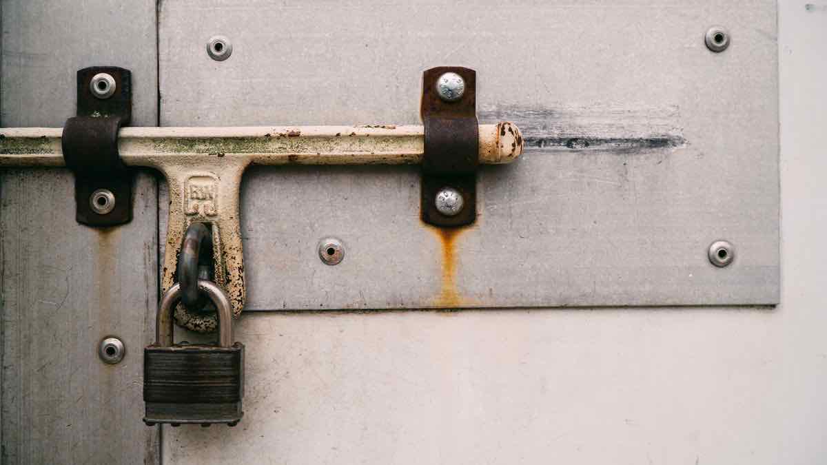 A steel door latch held shut by a padlock on a weathered grey metal door