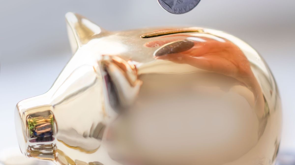 A coin dropping toward the slot of a gold piggy bank