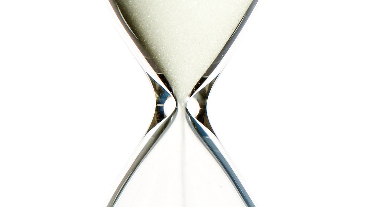 Close-up of an hourglass with pale sand running through its narrow neck against a white background