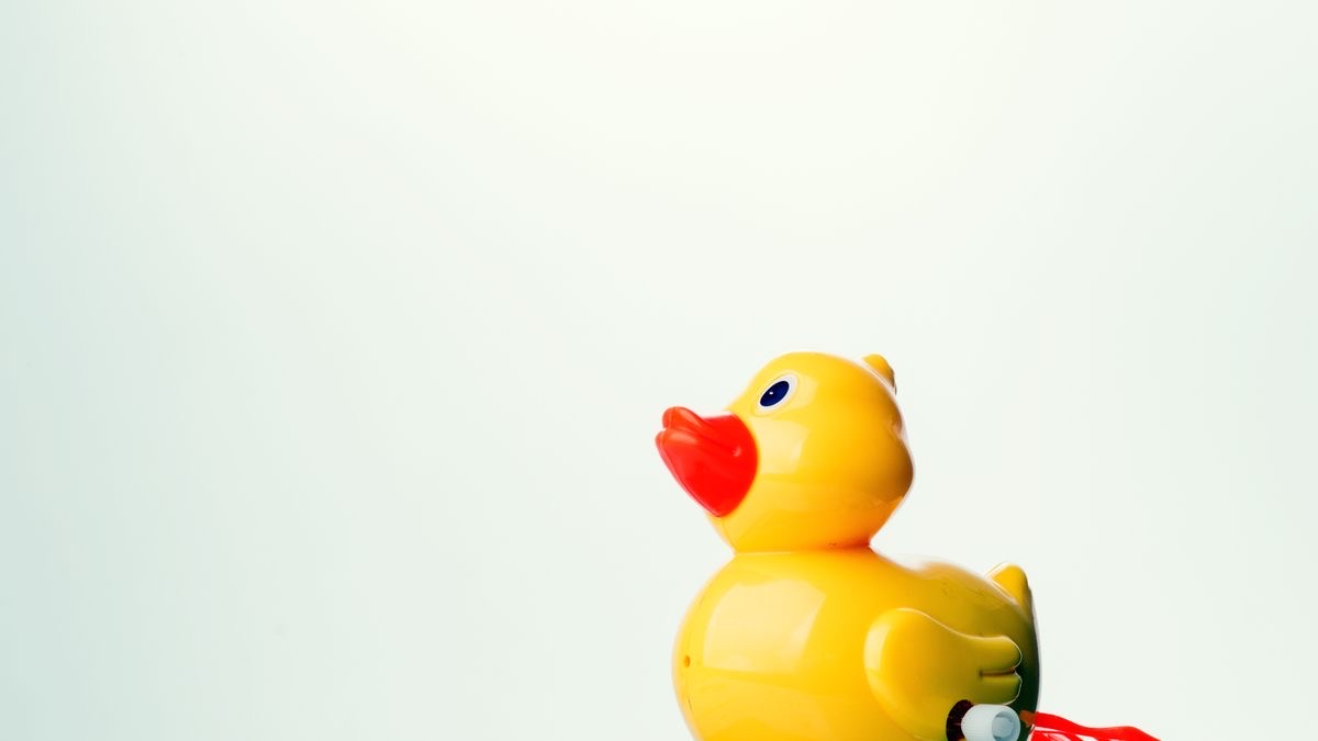 A yellow wind-up toy duck facing left against a plain pale background