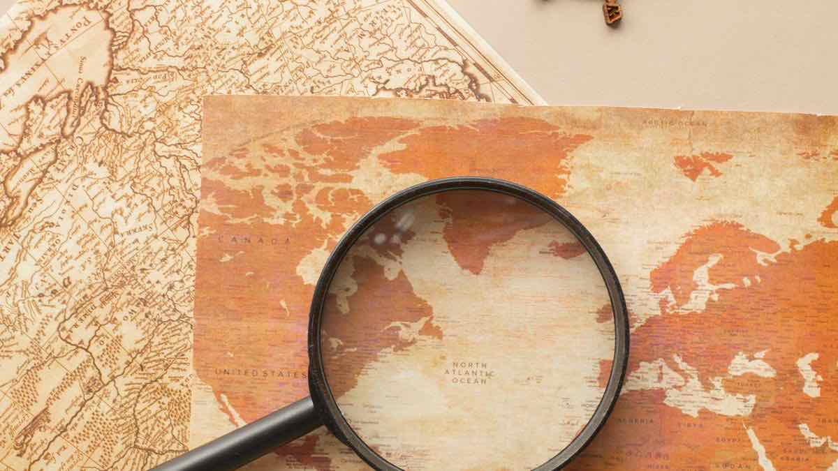 A black magnifying glass resting on a sepia-toned paper world map, enlarging part of the North Atlantic