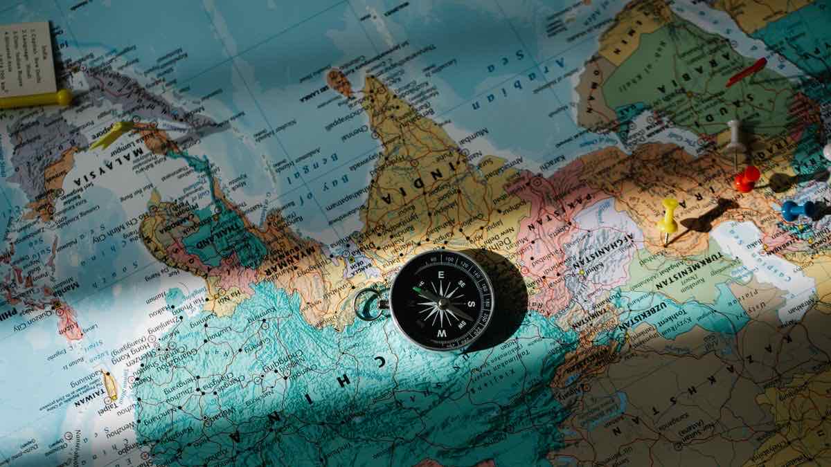 A small compass on a coloured world map with red, yellow and white pushpins pinned near the Middle East