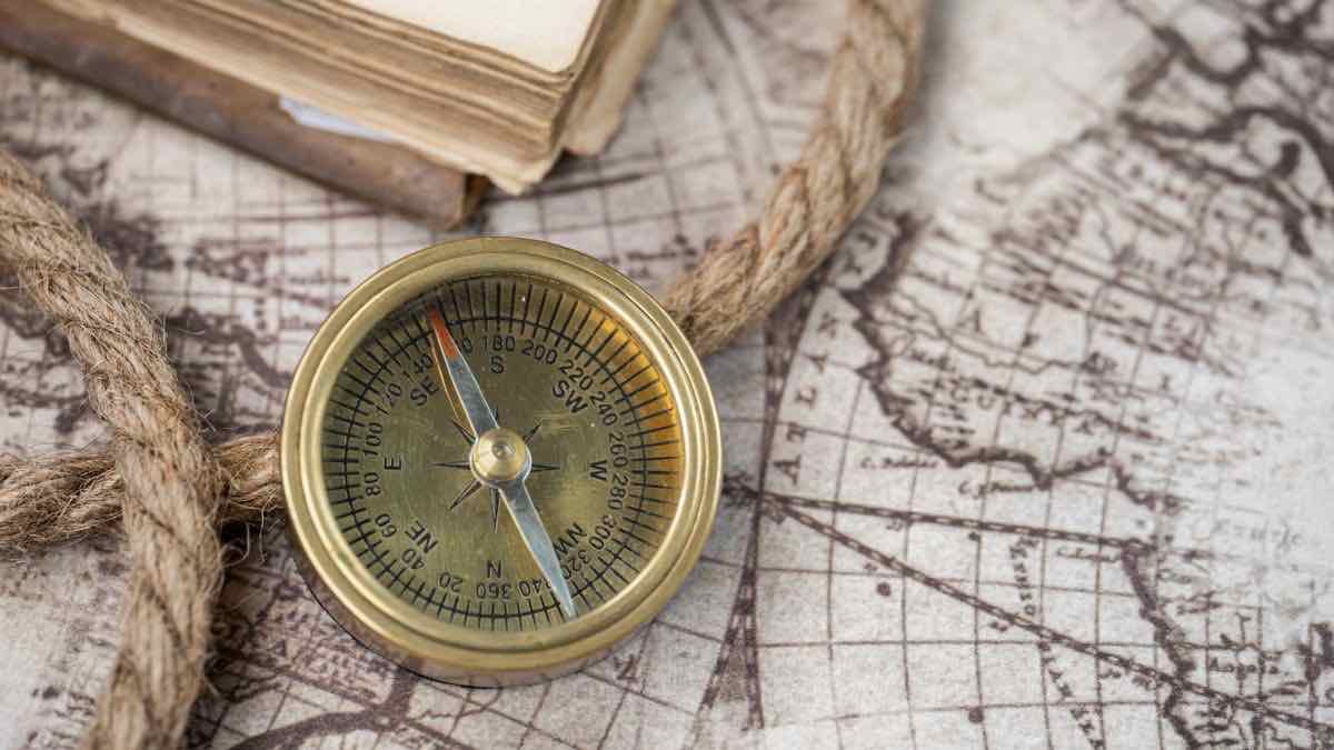 A brass compass resting on an antique world map beside a coil of rope and an old book
