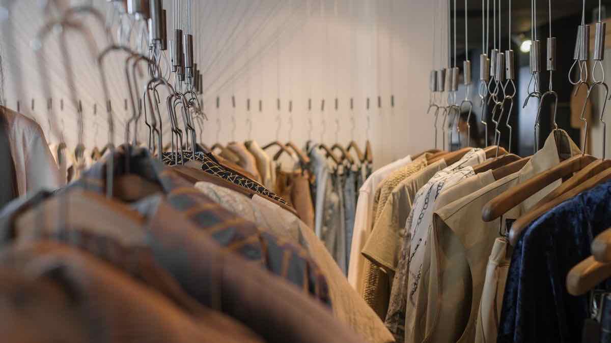 Rows of clothes on wooden hangers along a rail inside a boutique