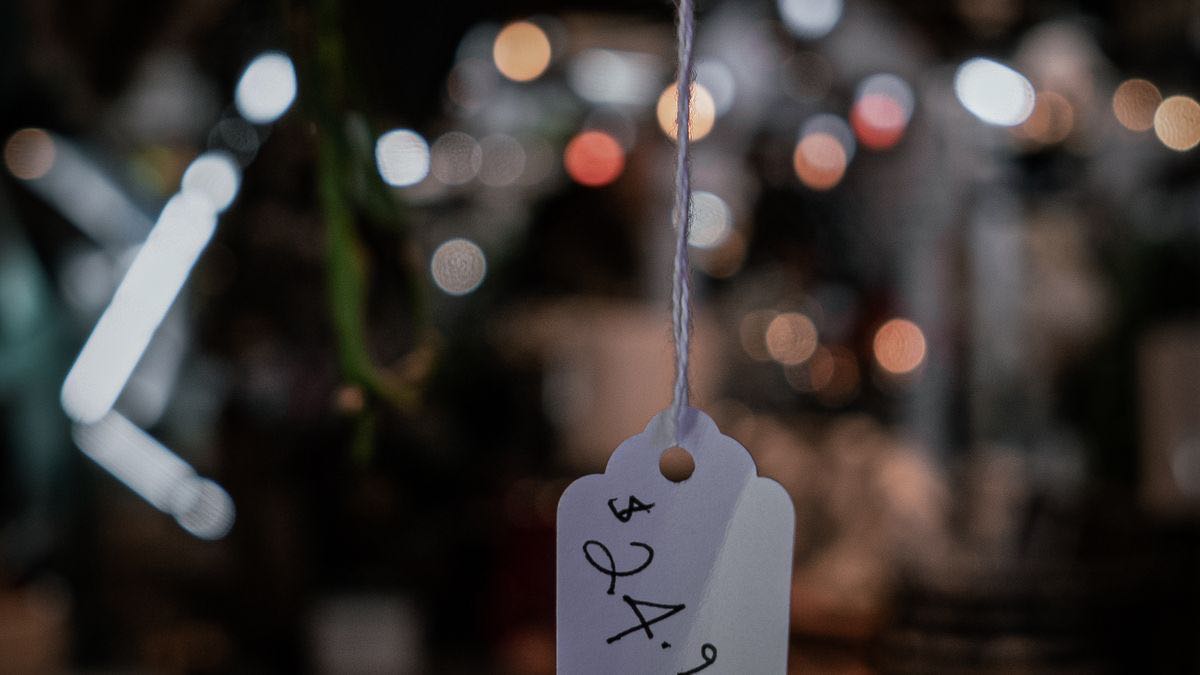 A white paper price tag on a string with a handwritten price, against a dark blurred background of lights