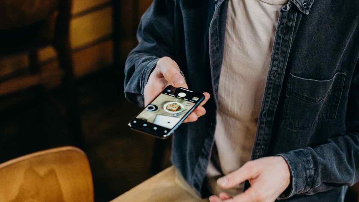 A man in a denim shirt holding a phone and framing a plate of food in its camera view