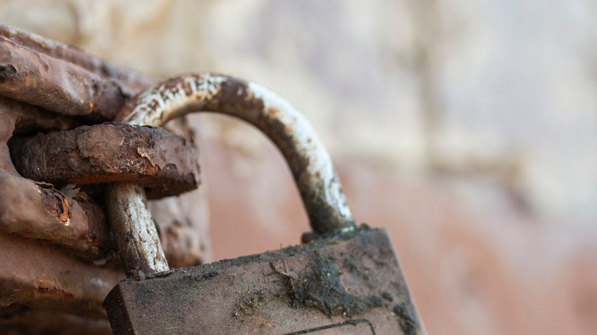 A rusty padlock hanging on a weathered metal chain, standing for gated access with a small free entrance