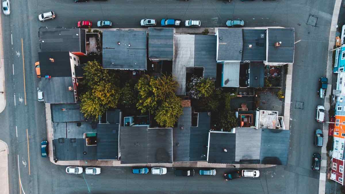 A drone view straight down on one city block of dark roofs and trees, ringed by streets and parked cars