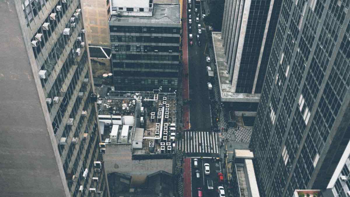 A narrow street seen from above, running between tall dark office buildings to a pedestrian crossing
