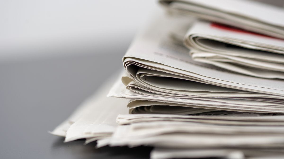 A tall stack of folded newspapers seen from the side on a dark table