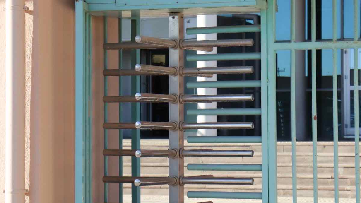 A steel turnstile inside a turquoise gate frame that lets one person through at a time, standing for access that is free but gated