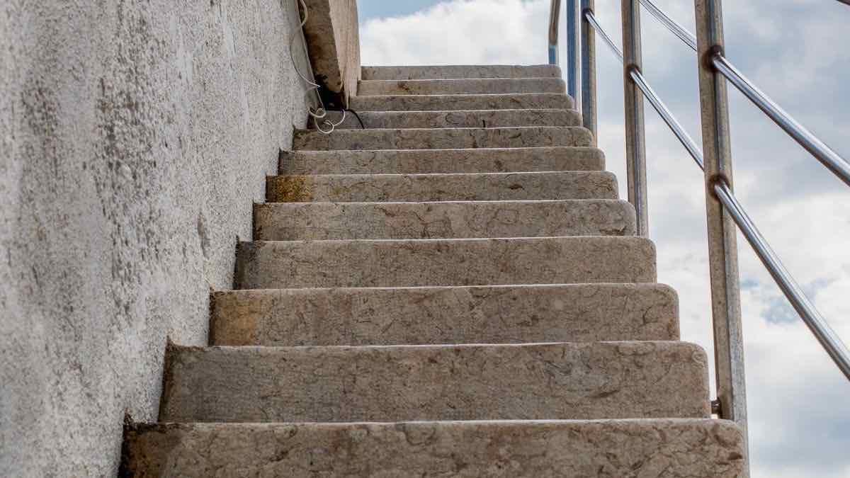 A flight of worn stone steps climbing toward a cloudy sky beside a steel handrail