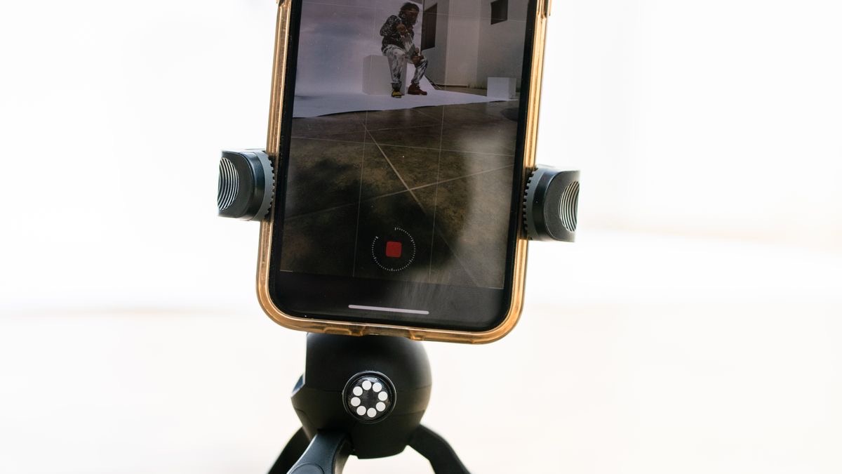 A smartphone clamped in a small black tripod showing a video recording screen