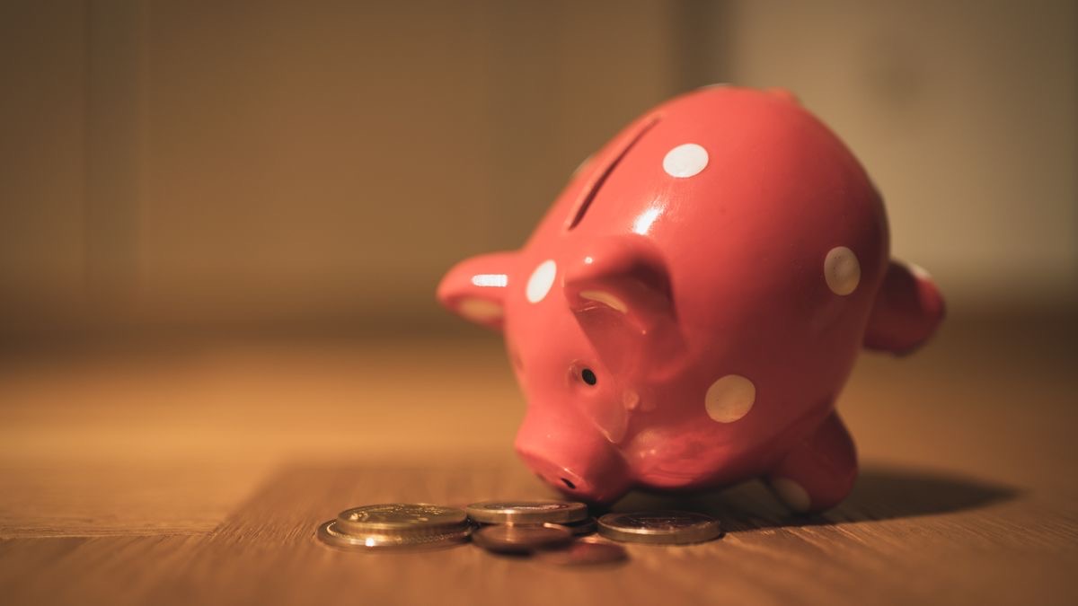 A red polka-dot piggy bank tipped forward on a wooden floor beside a small pile of coins