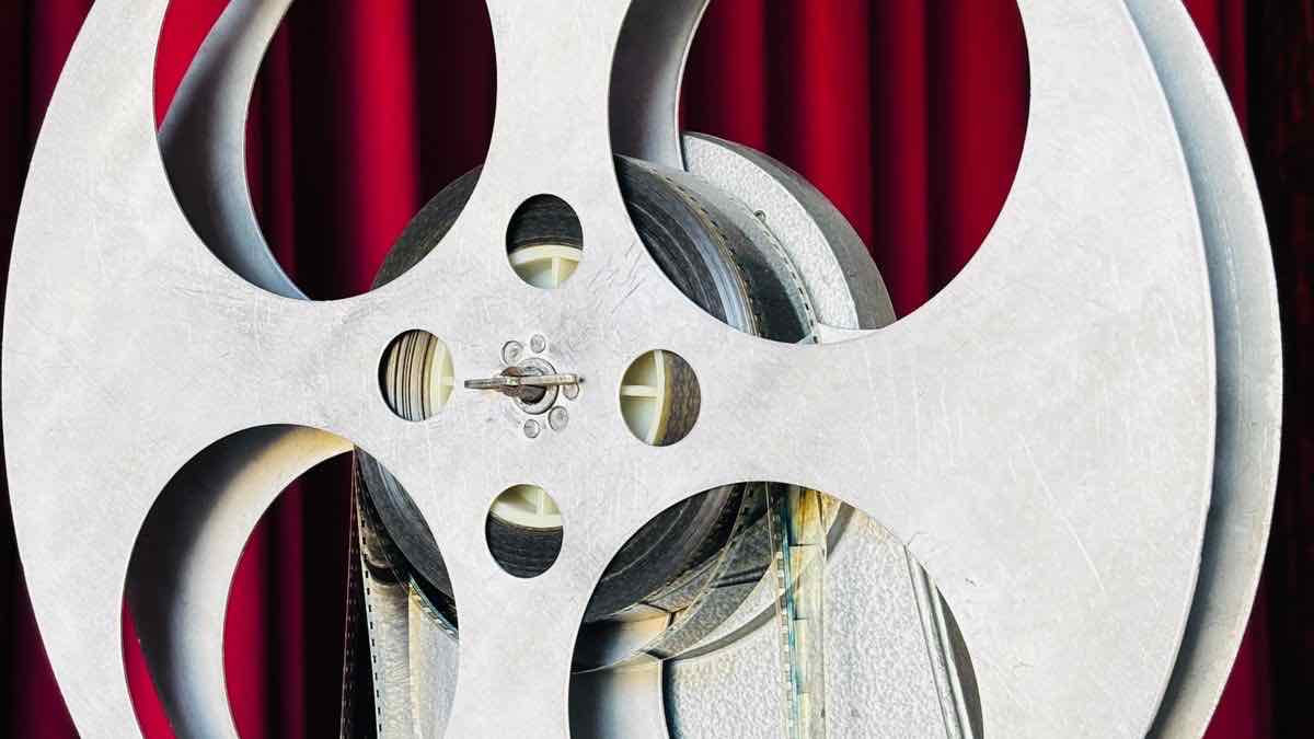 A large metal film reel in front of red theatre curtains