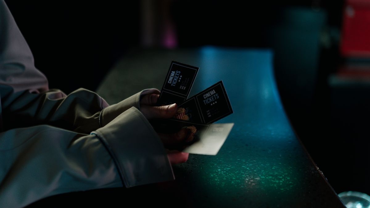 A hand holding three cinema tickets over a dark counter, standing for the paid entry that video search data usually needs