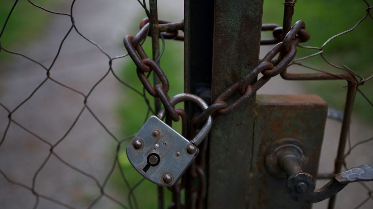 A weathered padlock and rusty chain securing a wire-mesh gate