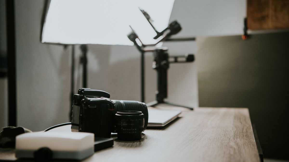 A desk with a camera and lens in front of softbox lights and a gimbal in a small video studio