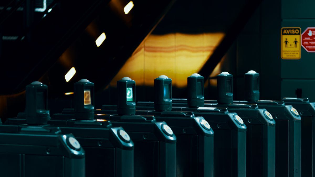A row of dark ticket gates in a subway station with one lit green, standing for paid access with a small free entry
