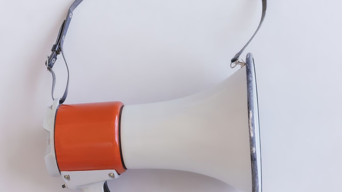 A retro megaphone with a shoulder strap lying on a plain white surface