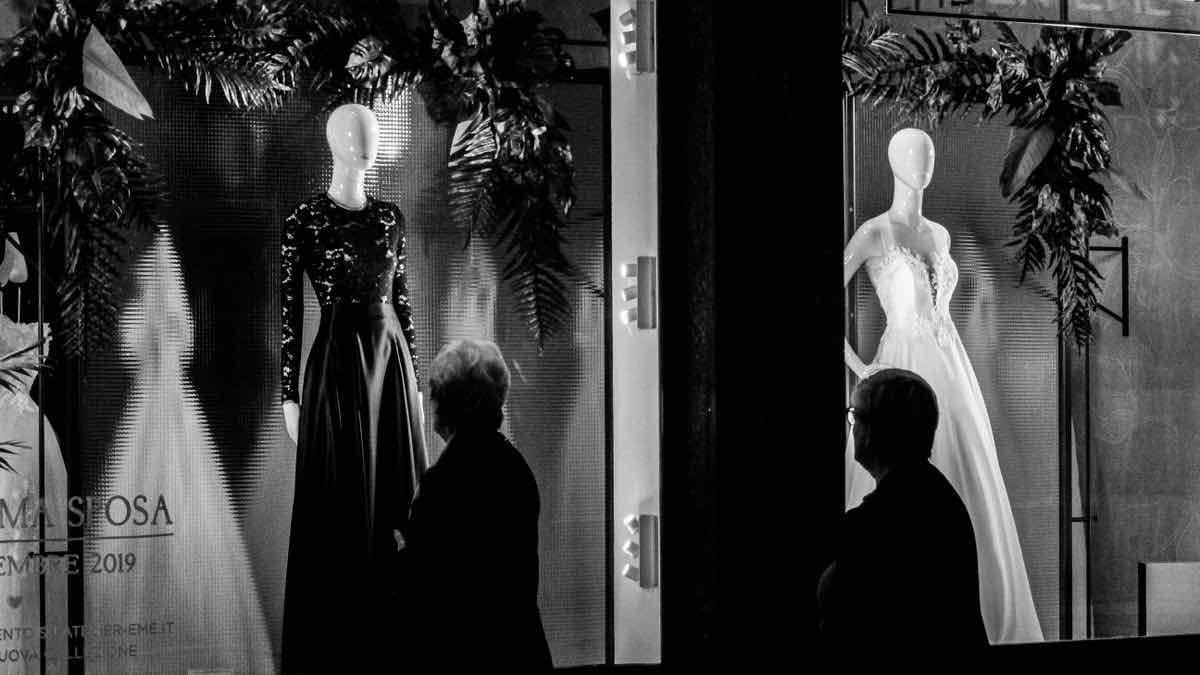 Two silhouetted figures looking into a brightly lit shop window at night without going inside
