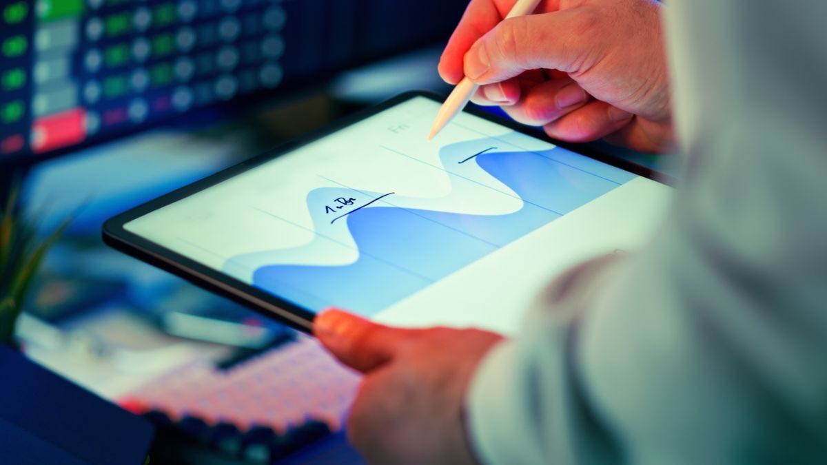 A hand using a stylus to annotate a rising and falling trend curve on a tablet screen