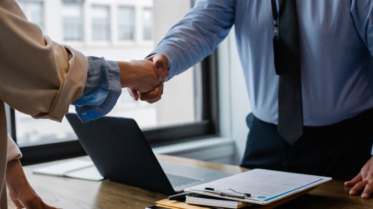 Two people shaking hands over a laptop and documents — the terms-of-service contract at the center of scraping disputes