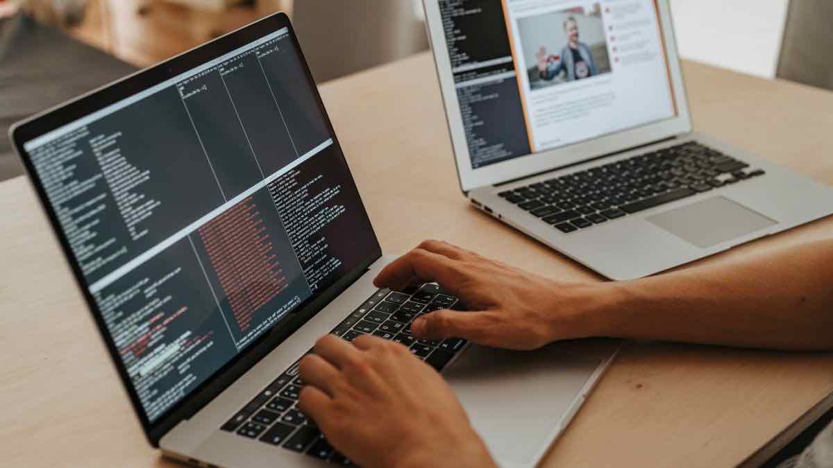 Two laptops on a desk, one running a terminal and one showing a profile — building the sourcing pipeline in code
