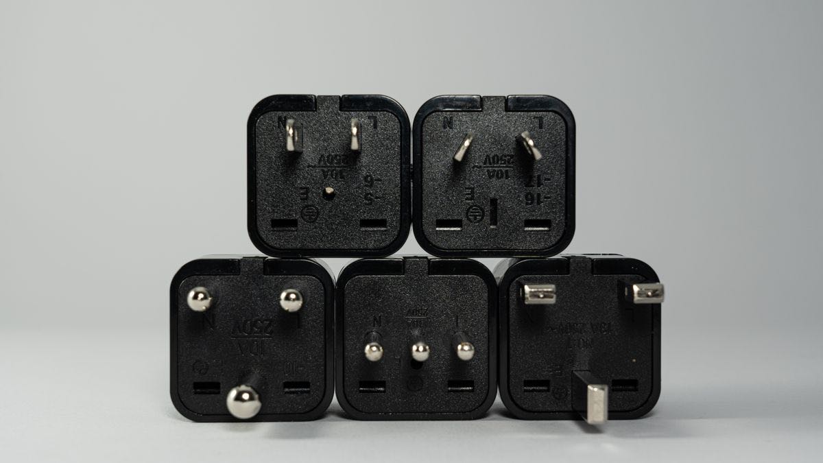 Five international plug adapters with different pin shapes lined up on a gray background