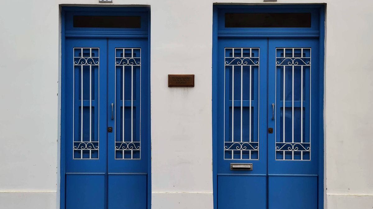 Two identical blue double doors set into the same white wall, each with its own separate house number