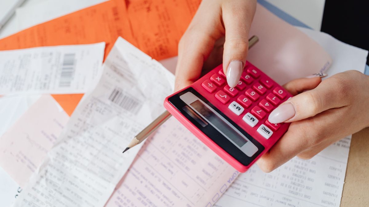 A hand using a calculator over a pile of receipts, representing the real cost of ScraperAPI credits per Google search