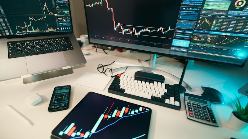 Multi-screen workspace with candlestick charts on a wide monitor and tablet, the kind of multi-pane data view a SERP dashboard delivers