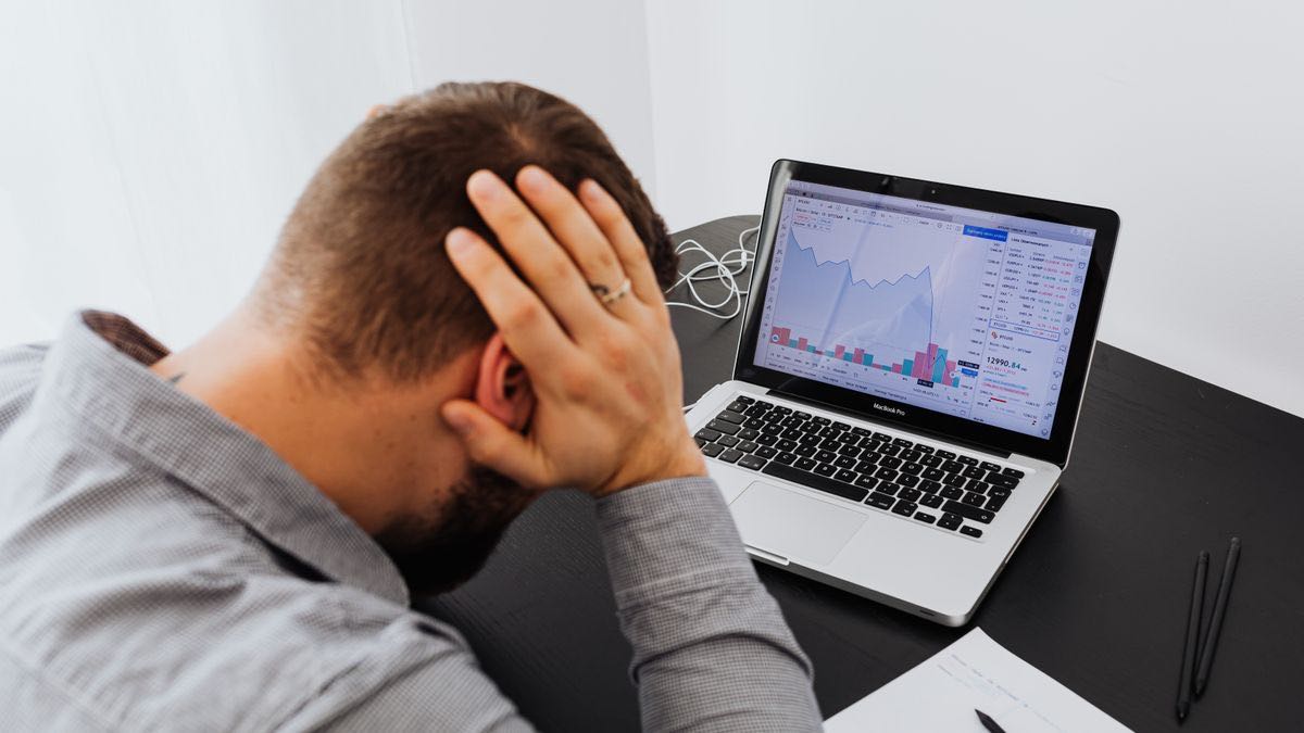 A developer holding their head in front of a laptop showing falling charts, the moment a batch of API calls fails