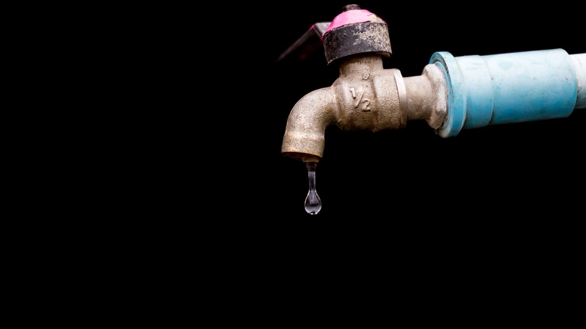 Old outdoor tap dripping a single drop of water against a black background