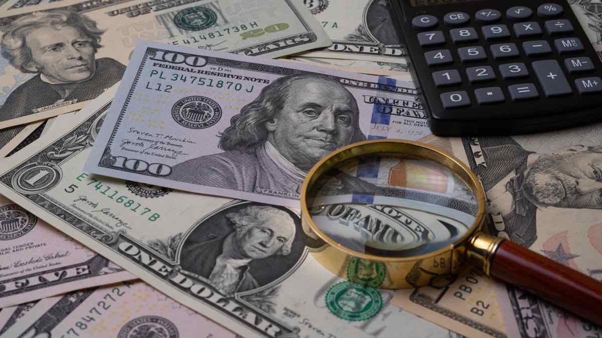 Magnifying glass and calculator resting on a spread of US dollar bills