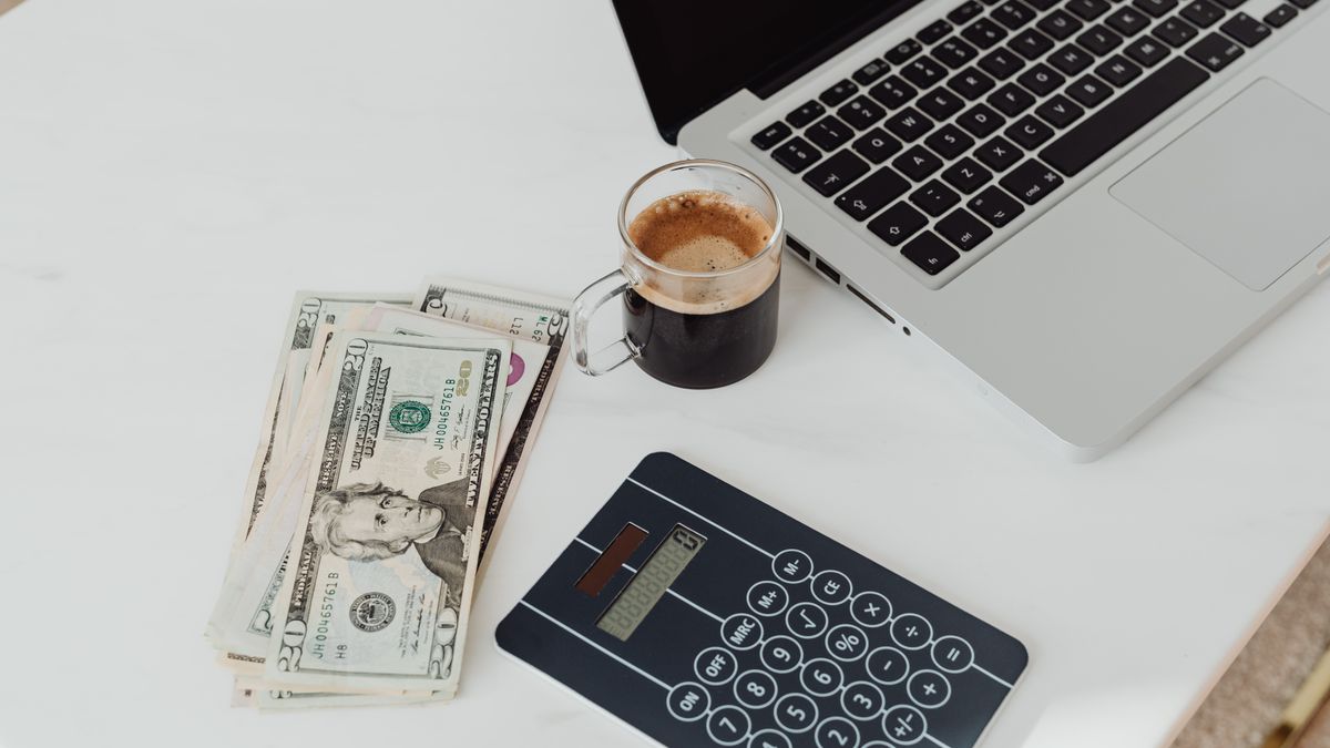 Laptop, US dollar bills and a calculator on a desk, illustrating SERP API cost comparison