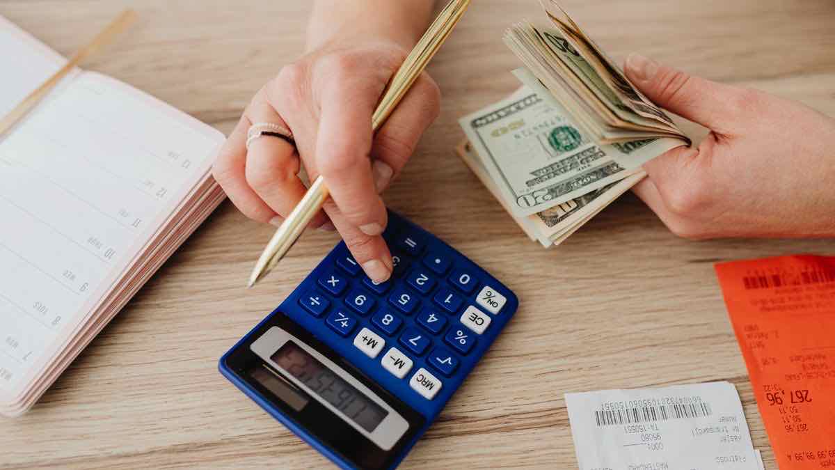 Hands counting dollar bills over a calculator and planner while budgeting a monthly API spend