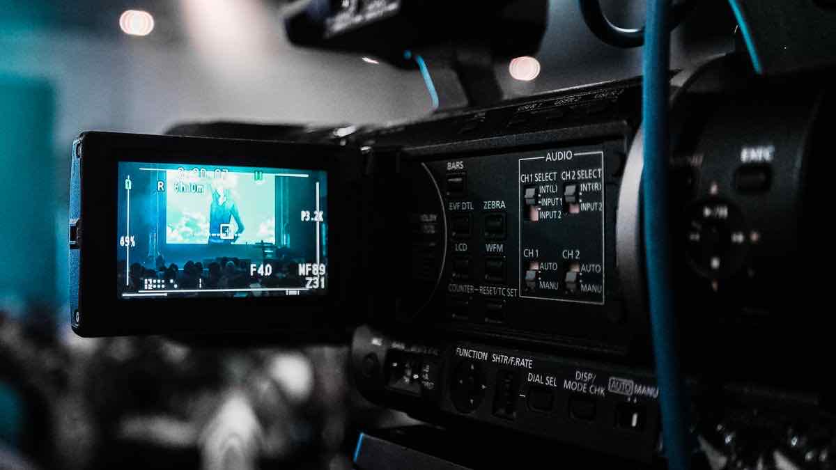 A professional video camera with its fold-out viewfinder screen showing a live recording