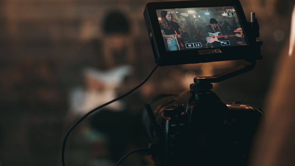 A camera field monitor showing two musicians being filmed, representing competitor video content production